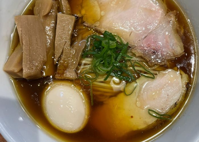 A close-up shot of a bowl of ramen at Ramen Touhichi, a Michelin star ramen restaurant in Kyoto. Pork, egg, bamboo shoots, spring onion and noodles are soaking in broth.